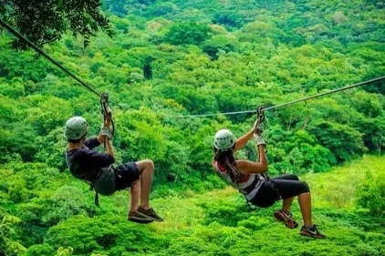 Two people ziplining over the rainforest canopy